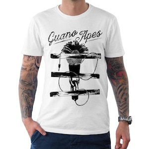 May include: White t-shirt featuring a black and white graphic of a microphone with a flower and the text "Guano Apes". The microphone is positioned between three horizontal wooden beams.