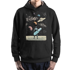 May include: Black hoodie with a graphic print of a figure with a surfboard in space. The design includes planets, stars, and a flying saucer. The sweatshirt has a front pocket and a drawstring hood.