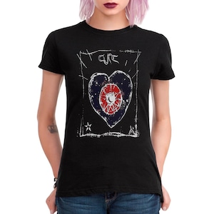 Puede incluir: Camiseta negra con un diseño gráfico desgastado. El diseño incluye una forma de corazón con un centro circular, una estrella y la palabra "CURE" en la parte superior. El gráfico es en blanco, rojo y azul.