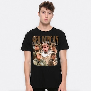 May include: Black t-shirt featuring a vintage-style graphic of a man and the text "Ser Duncan the Tall". The graphic includes multiple images of the same man in various poses. The shirt is a classic crew neck.