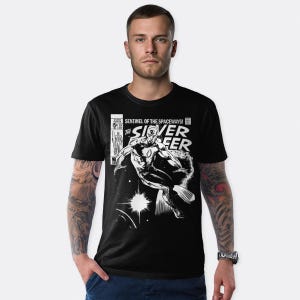 May include: Black t-shirt with a comic book illustration of the Silver Surfer. The design includes the text "Sentinel of the Spaceways!" and "The Silver Surfer" in white. The t-shirt has a crew neck.