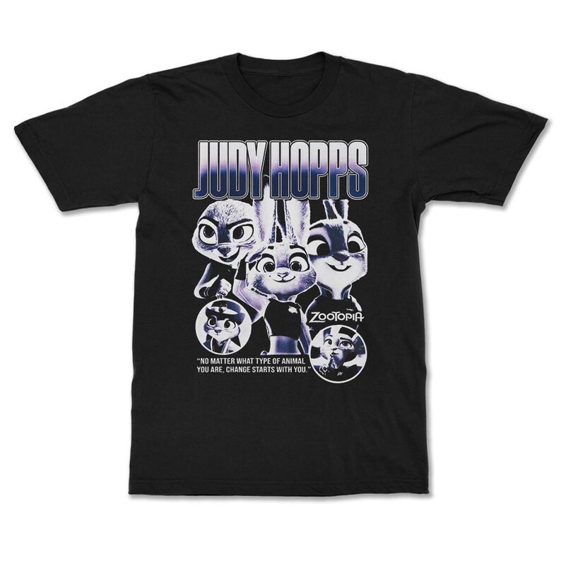 以下が含まれることがあります： 映画「ズートピア」のジュディ・ホップスのグラフィックがプリントされた黒いTシャツ。「JUDY HOPPS」の文字がグラデーションフォントでデザインされ、「どんな動物であっても、変化はあなたから始まる」という引用句が添えられています。