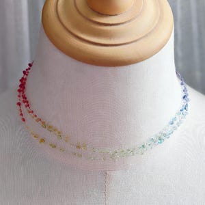 Puede incluir: Un collar de múltiples hilos con pequeñas cuentas de colores. Las cuentas hacen la transición del rojo al amarillo, al verde y al azul. El collar se exhibe en un busto de maniquí blanco.