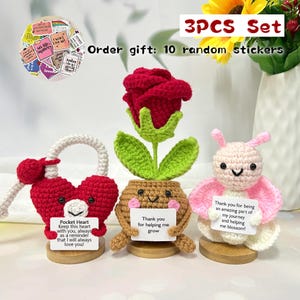 Puede incluir: Un conjunto de tres artículos de ganchillo: un candado de corazón rojo, una rosa roja en una maceta y un conejito rosa. Cada artículo tiene una base de madera y un pequeño letrero con texto. El conjunto incluye 10 pegatinas aleatorias.