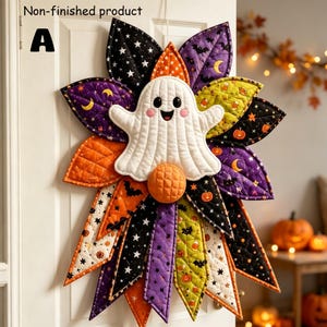 Puede incluir: Un producto no terminado para colgar en la pared que presenta un fantasma blanco central con cara sonriente y mejillas rosadas, rodeado de pétalos de tela acolchada en negro, naranja, morado y verde, decorados con patrones de estrellas, lunas, murciélagos y calabazas.