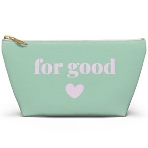 May include: A mint green zippered pouch with the words "for good" in light purple, and a small purple heart. The pouch has a gold-colored zipper and a white interior. The bag is designed to hold small items.