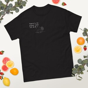 May include: Black t-shirt with the text "There's no place like 127.0.0.1" and a graphic of a house and code. The shirt is made of a soft material and is a comfortable fit. The design is printed in white.