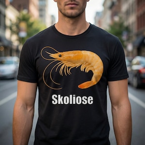 May include: Black t-shirt featuring a large, realistic image of a cooked shrimp in shades of orange and yellow. The word "Skoliose" is printed in white below the shrimp graphic.