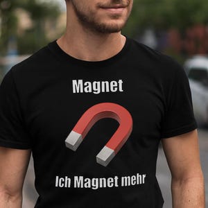 May include: Black t-shirt with the word "Magnet" in white above a red horseshoe magnet with gray ends. Below the magnet, the text "Ich Magnet mehr" is printed in white.