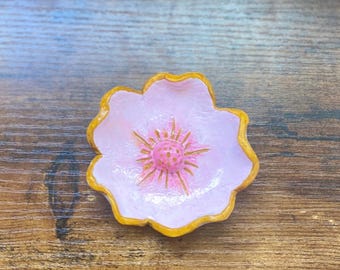 May include: A pink flower-shaped dish with a gold rim. The center of the dish has a pink flower design with gold accents.