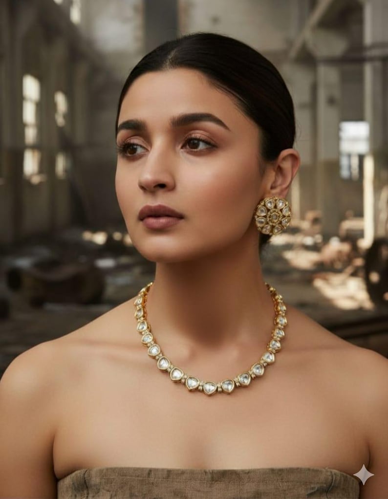 May include: A woman wearing a gold necklace and matching earrings. The necklace features clear, heart-shaped stones set in a gold frame. The earrings are round with a similar design. The woman has dark hair and is wearing a strapless top.