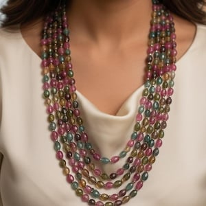 Op de afbeelding: Een meerlagige ketting met ovale kralen in roze, groen en goud. De kralen worden gescheiden door kleine zilverkleurige afstandhouders. De ketting wordt gedragen tegen een witte achtergrond. Een opvallend sieraad.