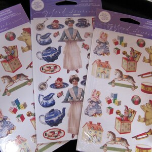 Peut inclure: Trois paquets de feuilles d'autocollants sans acide et sans lignine. Chaque feuille présente des illustrations de style vintage de jouets, de poupées, de services à thé et de femmes en robes. Les autocollants sont de couleurs variées, dont le bleu, le rouge et le jaune.
