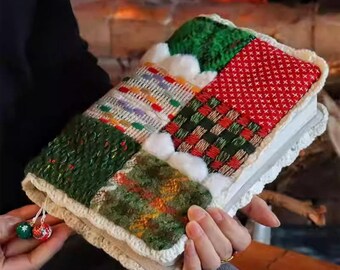 May include: A colorful, patchwork-style book cover with a white crocheted border. The cover features various textured fabrics in green, red, and white, with small pom-poms and decorative tassels. The overall theme is cozy and handcrafted.