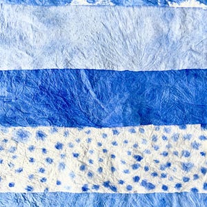 May include: Abstract artwork featuring horizontal bands of varying shades of blue and white. The textures range from smooth to heavily textured, with some sections displaying a spotted pattern. The overall effect is a watercolor-like appearance.