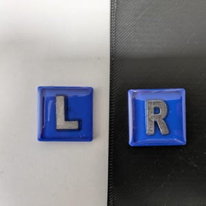 May include: Two blue square tiles with silver letters. The left tile has the letter "L" and the right tile has the letter "R".