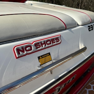 May include: A white boat with red trim and a "NO SHOES" sign. The boat has a silver railing and a black and red stripe on the side. The boat is labeled "23 LSV".