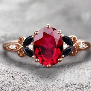 May include: A rose gold ring with a large red gemstone surrounded by smaller white and black gemstones.
