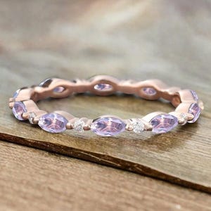 May include: A rose gold eternity band with a row of marquise-shaped amethyst gemstones and small round diamonds.