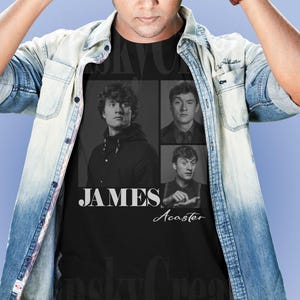 May include: Black t-shirt featuring a collage of three images of James Acaster, with the name "JAMES" in white block letters and "Acaster" in script. The shirt is worn by a person wearing a denim shirt.