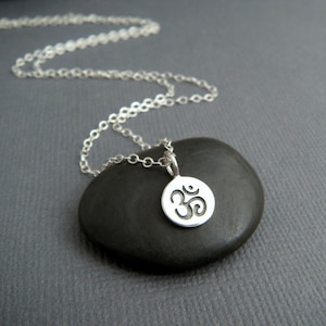 May include: A silver chain necklace with a small, round pendant featuring the Om symbol. The pendant is engraved with the symbol and hangs from a delicate chain.
