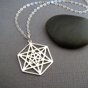 May include: A silver necklace with a geometric pendant featuring a complex, intricate design. The pendant is shaped like a hexagon with a star-like pattern inside.