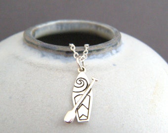 May include: A silver necklace with a pendant shaped like a surfboard and paddle. The pendant has a swirl design on the surfboard.