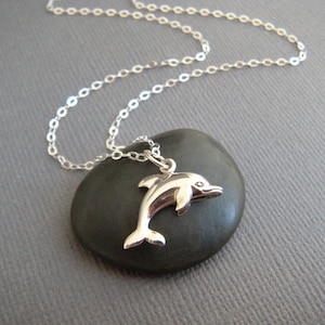 May include: A silver chain necklace with a silver dolphin pendant. The dolphin is leaping out of the water.