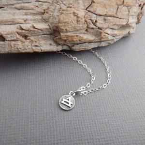 May include: A silver necklace with a small, round pendant featuring a geometric design. The pendant is on a delicate silver chain.
