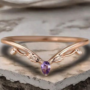 May include: A rose gold ring with a delicate, nature-inspired design. The ring features a teardrop-shaped purple gemstone at the center, flanked by leaf-like details and small white accents. The band curves gracefully, creating an elegant, feminine aesthetic.