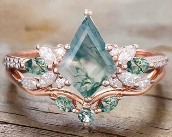 Peut inclure: Une bague de fiançailles en or rose avec une pierre centrale en agate mousse et un délicat motif floral. La bague présente une pierre unique en forme de cerf-volant avec un motif vert et blanc.