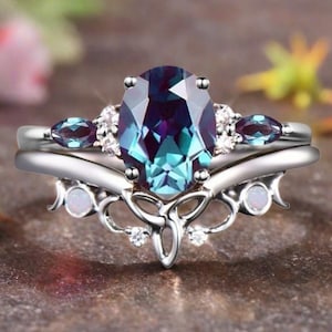 Peut inclure: Un ensemble de bagues en argent avec une pierre précieuse ovale changeant de couleur, aux teintes bleues et violettes. La bague est ornée de petites pierres précieuses et d'une bande décorative, présentant un design classique et élégant.