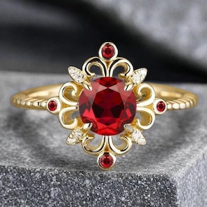 May include: A gold ring with a large red gemstone surrounded by smaller red gemstones and white diamonds. The ring has a delicate, ornate design.
