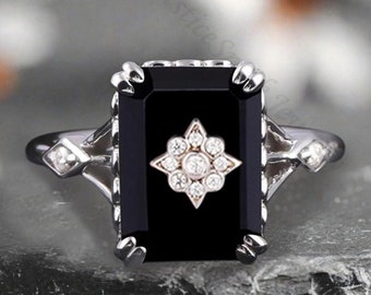 May include: A silver ring with a black rectangular gemstone and a star-shaped cluster of smaller diamonds in the center.