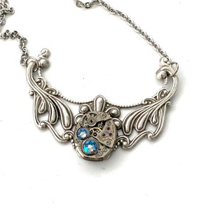 May include: Silver necklace with a delicate filigree design and a vintage watch face pendant with blue crystals.