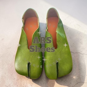 Può includere: Un paio di scarpe in pelle verde con punta divisa. Le scarpe hanno un design unico con una sezione separata per l'alluce. L'interno è arancione. Il testo "ARS Shoes" è visibile.