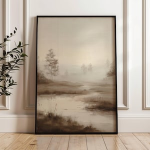 May include: A framed landscape painting in muted tones, depicting a misty marsh scene with trees and water. The artwork has a soft, diffused light and a black frame. The overall aesthetic is calm and natural, with a focus on the natural world.