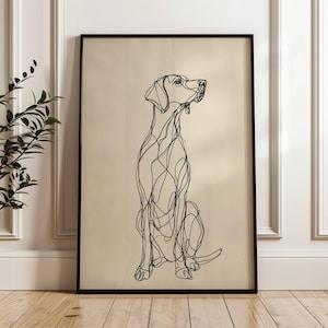 May include: Black framed art print featuring a minimalist line drawing of a dog in a seated position. The dog is depicted with continuous black lines on a beige background. The artwork is displayed in a room with white trim and a wooden floor.