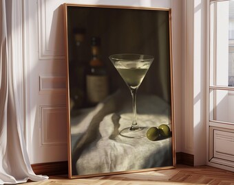 May include: A martini glass filled with a clear liquid sits on a white linen cloth with two green olives. The glass is on a wooden table with a bottle of liquor in the background.