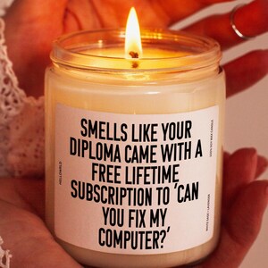 May include: A white candle with a black label that reads "Smells like your diploma came with a free lifetime subscription to 'Can you fix my computer?'".