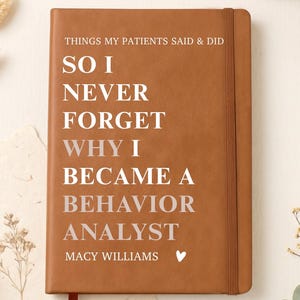 May include: A tan notebook with an elastic closure and a ribbon bookmark. The cover features white text that reads: THINGS MY PATIENTS SAID & DID SO I NEVER FORGET WHY I BECAME A BEHAVIOR ANALYST MACY WILLIAMS with a small white heart icon.