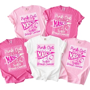 May include: Five short-sleeved t-shirts in shades of pink and white, each featuring a graphic print with a pennant design, a football, a ribbon, and the text "Pink Out MASCOT Tackle Breast Cancer" over a vertical striped background pattern.