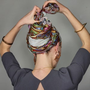 May include: A person wearing a gray dress with a low back and a colorful patterned headscarf. They are wearing large wooden earrings.