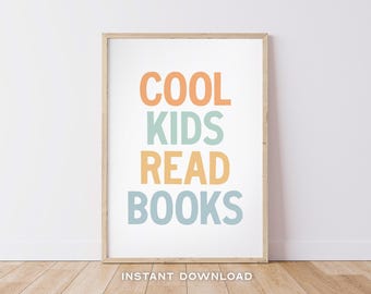 May include: A printable poster with the text "COOL KIDS READ BOOKS" in a rainbow color scheme of orange, blue, and yellow. The poster is framed in a light wood frame and is sitting on a wooden floor.