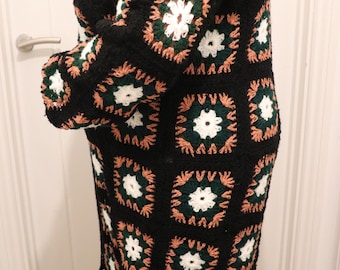 Puede incluir: Un cárdigan largo de crochet negro con un patrón de cuadrados de la abuela en tonos de verde, blanco y melocotón.