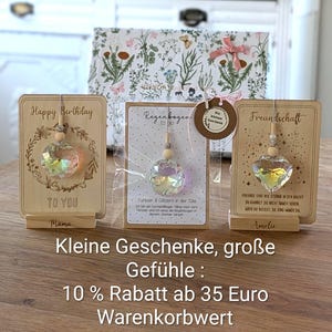 May include: Wooden gift cards with crystal ornaments. One card says "Happy Birthday" with a floral wreath. Another says "Regenbogen to go" and the last says "Freundschaft". A gift box with floral design is in the background.