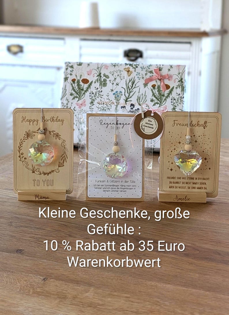 May include: Wooden gift cards with crystal ornaments. One card says "Happy Birthday" with a floral wreath. Another says "Regenbogen to go" and the last says "Freundschaft". A gift box with floral design is in the background.