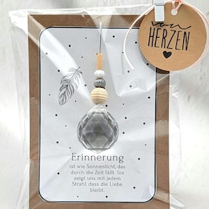 Könnte beinhalten: Ein klarer Kristallprismen-Ornament mit Holzperlen und einem silbernen Faden, verpackt in einer transparenten Plastiktüte. Die Karte im Inneren hat eine Federillustration und das Wort "Erinnerung". Ein kleines Etikett sagt "von Herzen".