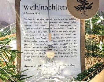 May include: A Christmas-themed gift set featuring a clear glass ornament with a decorative wooden bead and a small round tag with a Christmas tree illustration. The set is presented in a box with text in German.