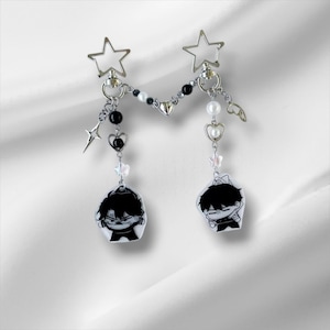 Może przedstawiać: Srebrna bransoletka z dwoma czarno-białymi zawieszkami z postaciami z kreskówek, czarno-białymi koralikami, srebrnymi gwiazdami i srebrnymi sercami.